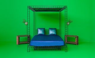 A striking four poster bed with a steel grid structure and metallic blue bed covers against a bright green wall and floor.