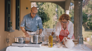 stanley tucci standing near two pots on a stove at an italian villa in the tv show searching for italy