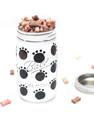A mason jar decorated with black and white chalk paint decor and filled with dog treats