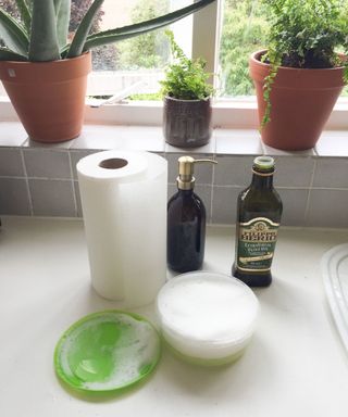 plastic container on countertop filled with soapy water, being cleaned with tiktok hack - with a jug of oil and plants in the background