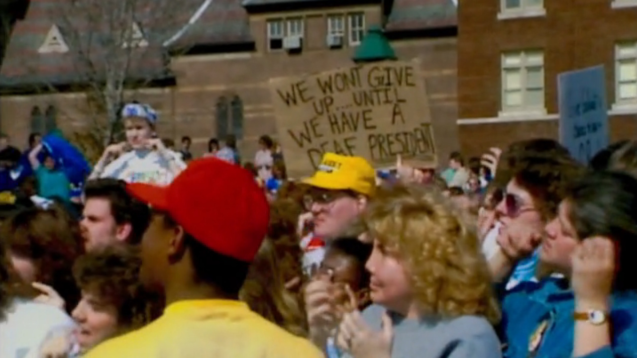 ドキュメンタリー「Deaf President Now!」で紹介されたこの看板には、「聴覚障害者の大統領が誕生するまで私たちは諦めない」と書かれている。 1988年にギャローデット大学の学生が抗議活動を行っている様子が描かれている。