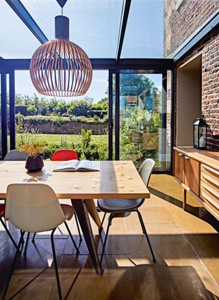 pale wood dining table with colored chairs and bifold doors open to garden midcentury sideboard