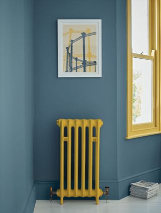 Tall thin traditional radiator painted mustard yellow against a dark blue wall