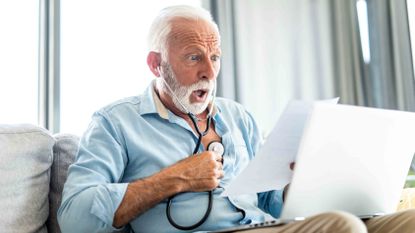 older man with stethoscope to his chest, looking at medical bill in shock