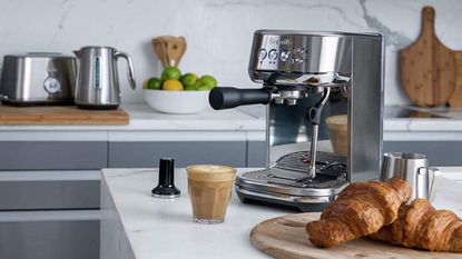 Breville Bambino Plus espresso machine on a countertop with coffee croissants and other kitchen utensils around