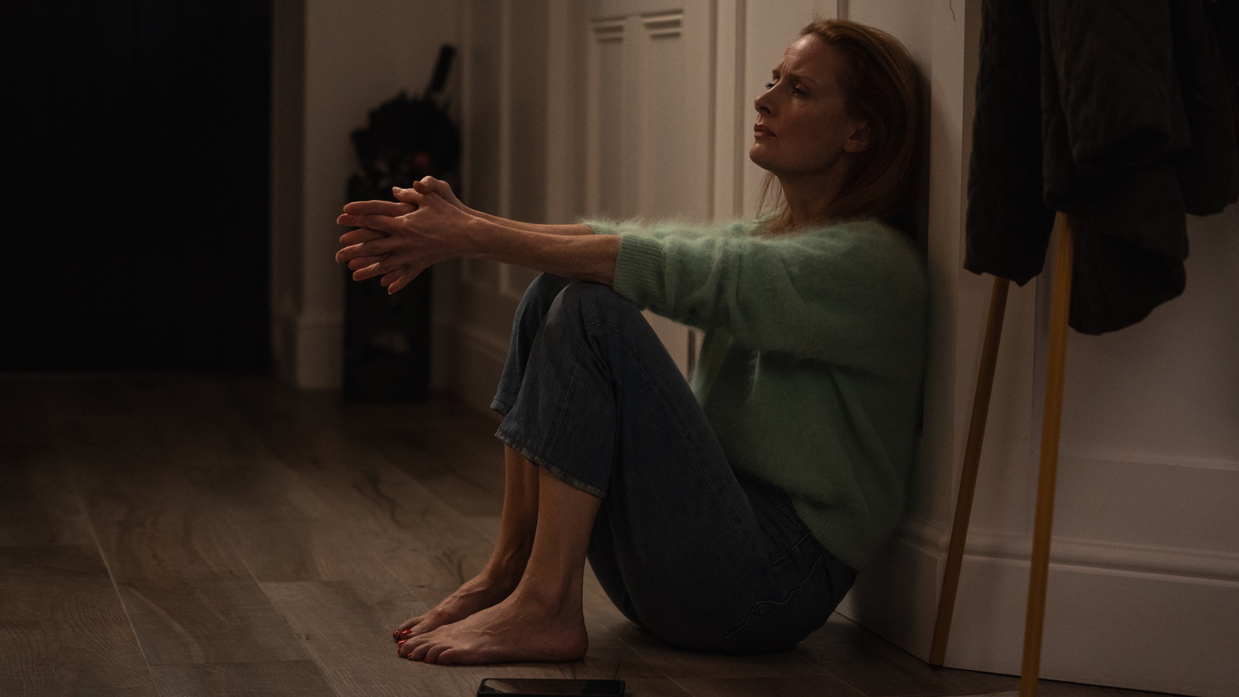 Kate in a fluffy green jumper and jeans sitting on the floor and looking upset