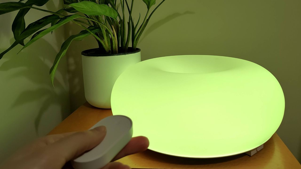 IKEA Varmblixt lamp illuminated yellow-green, with person's hand holding remote control