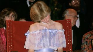 Princess Diana with her head slumped as she falls asleep at an event in an off the shoulder organza gown in light blue