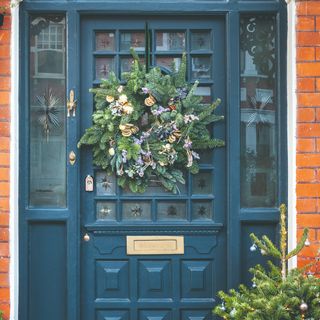 An ornamental blue front door with glass inserts decorated with a Christmas wreath hung on a velvet ribbon