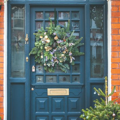 An ornamental blue front door with glass inserts decorated with a Christmas wreath hung on a velvet ribbon