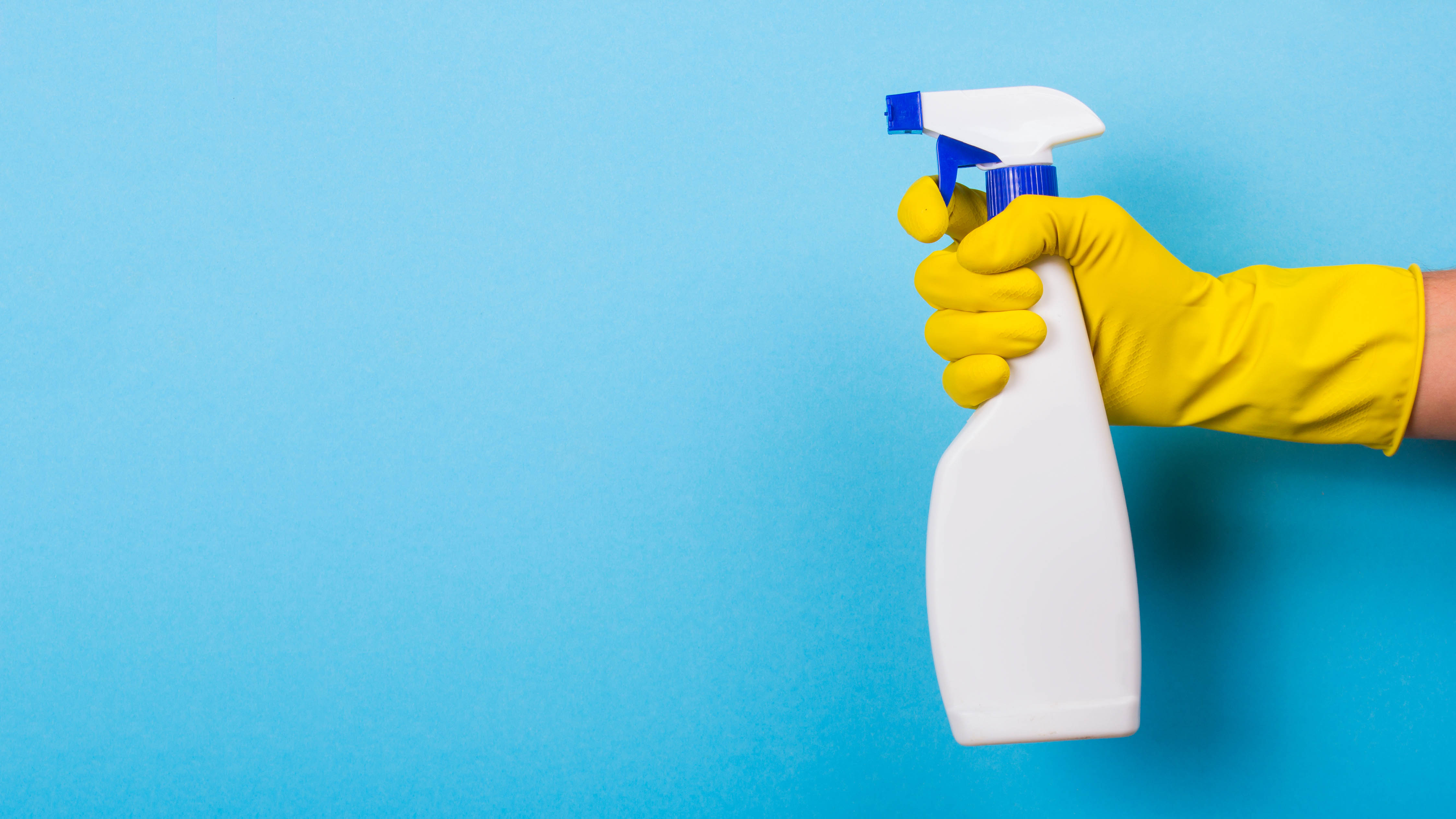 An unlabelled spray bottle being held by a gloved hand on a blue background