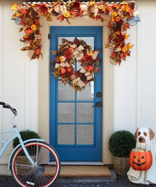 Blue front door with Halloween autumnal garland and matching wreath with dog figurine holding treat or treat candy bucket