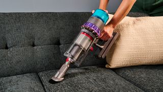 Dyson Gen5 Detect vacuum cleaner in handheld mode, being used on a sofa