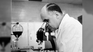 Black and white photo of Dr. Maurice Hilleman, Director of virus and cell biology research, Merck Institute of Therapeutic research at West Point, looking through a microscope to check the growth of a virus in roller tube tissue culture (March 7, 1963).