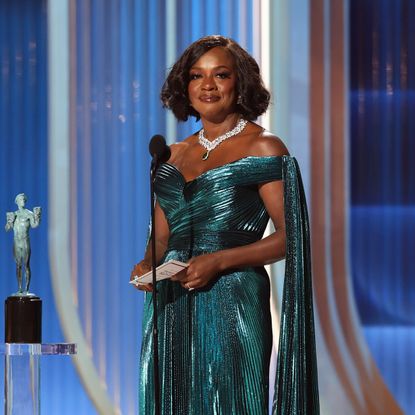 a black woman wears a teal gown while presenting at an awards show