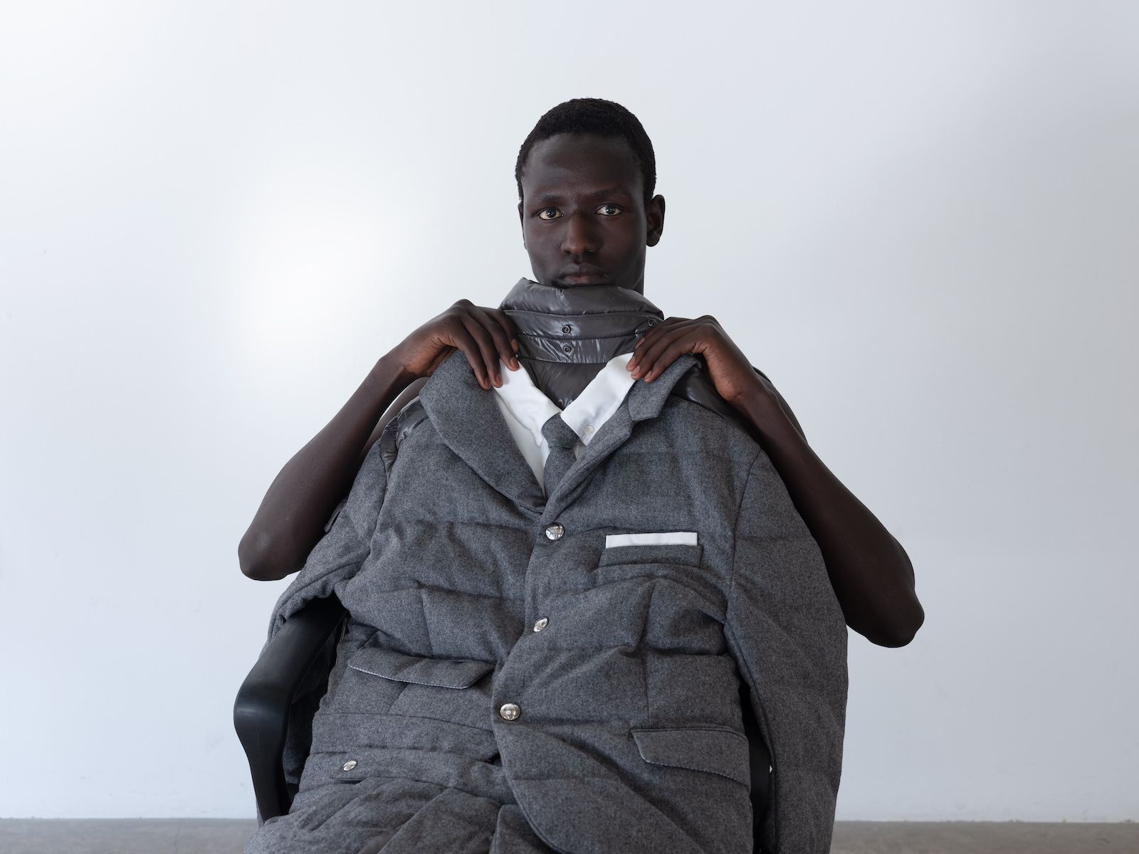 Man holds up puffer jacket which has the appearance of a suit jacket, shirt and tie