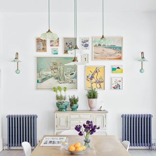 Dining room with gallery wall and wall and pendant lights with blue and green glass shades