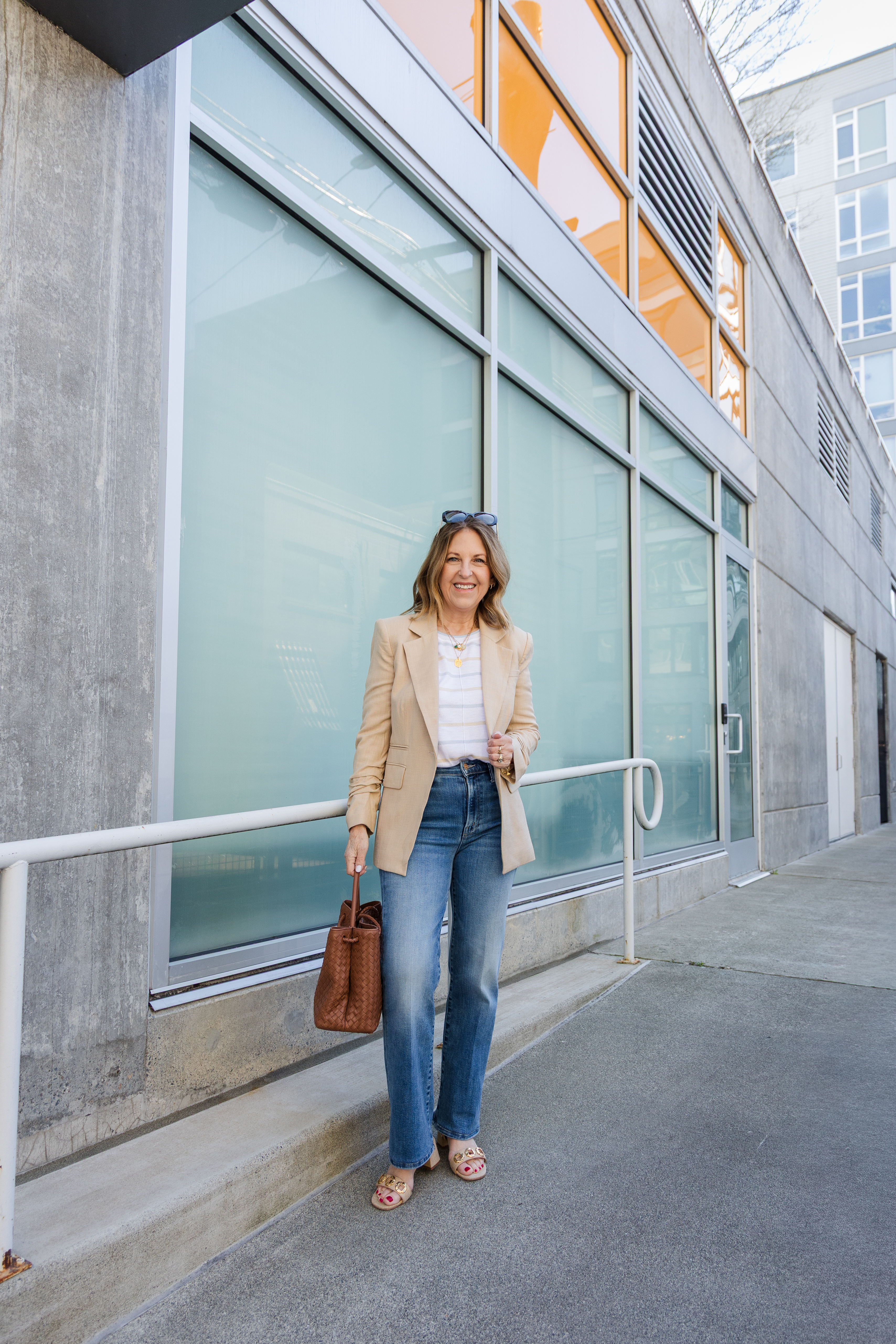 A former VIP Nordstrom stylist wearing a tan blazer over a white tee, jeans, and tan heels.