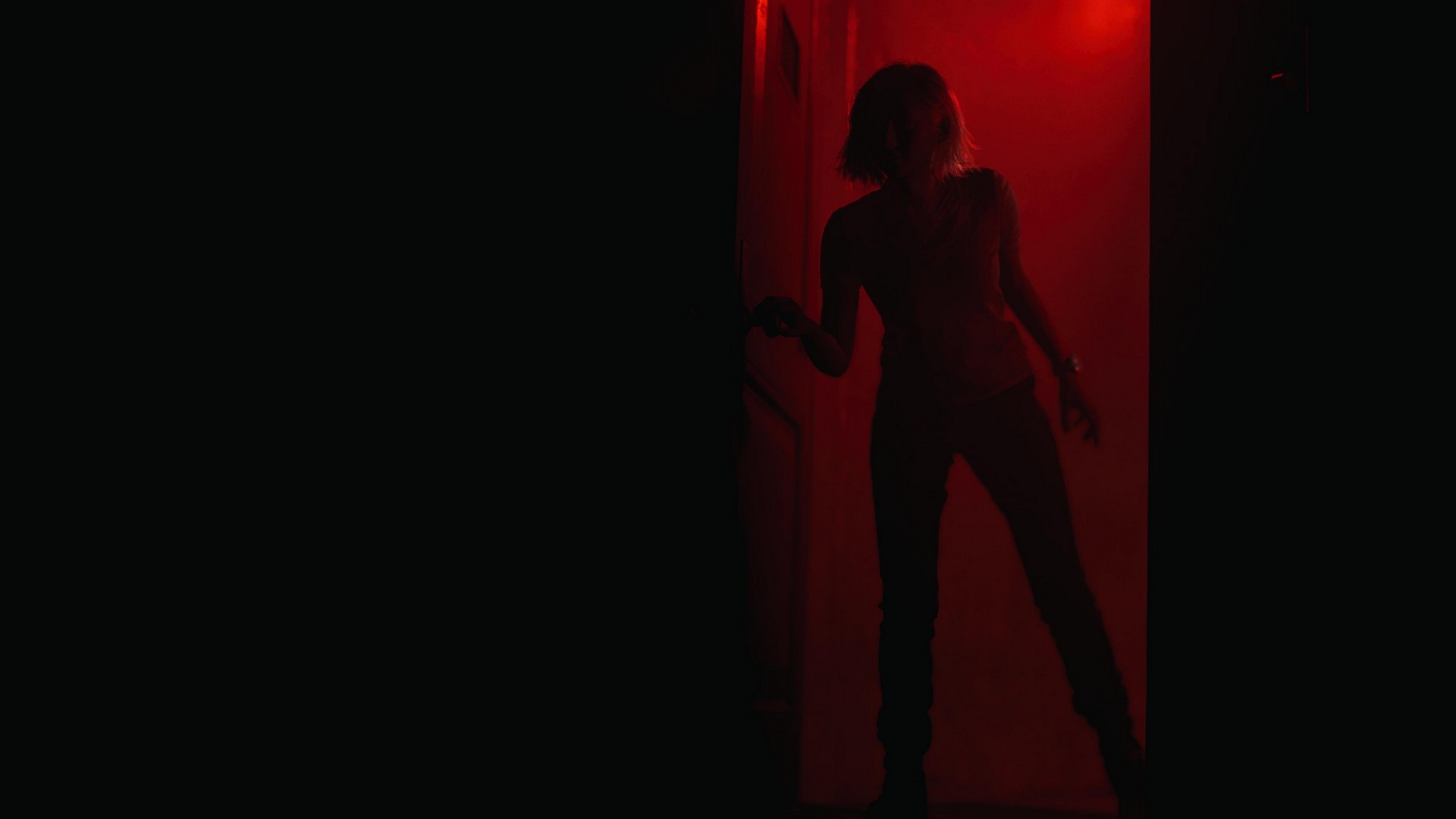 Grace enters a pitch black room in Resident Evil Requiem, silhouetted by harsh red behind her