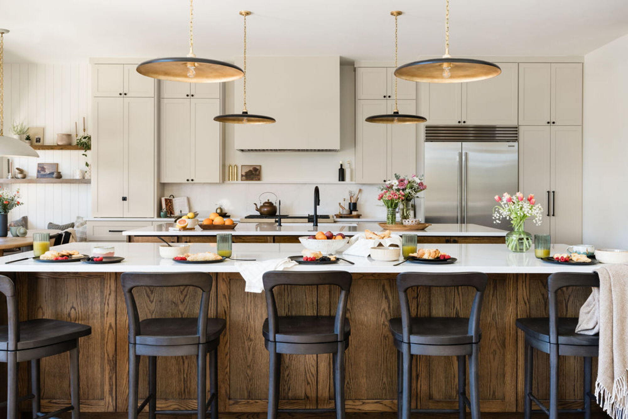 A kitchen with a large island, bar stools, and large bronze pendant lights