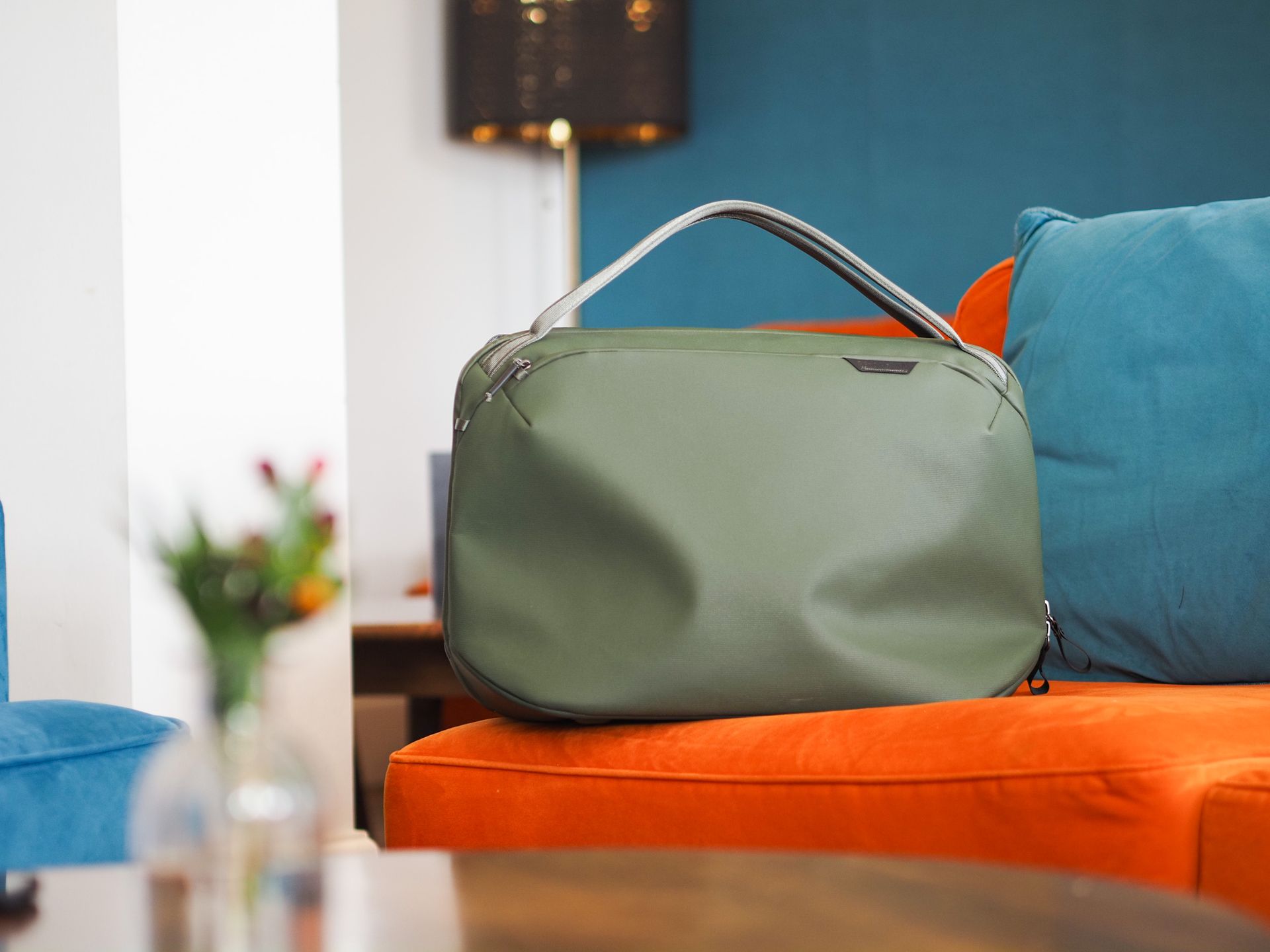 Peak Design Travel Weekender 25L bag in sage green, on a bright orange sofa