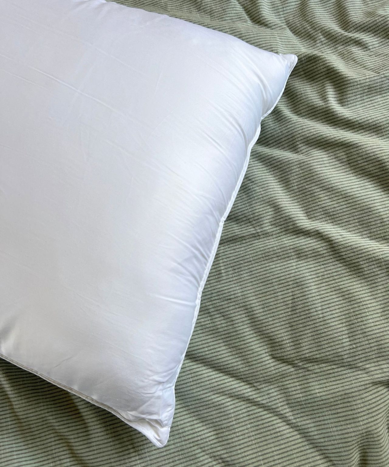 Cozy Earth Bamboo Down Alternative Pillow pictured on a green striped bedding set.