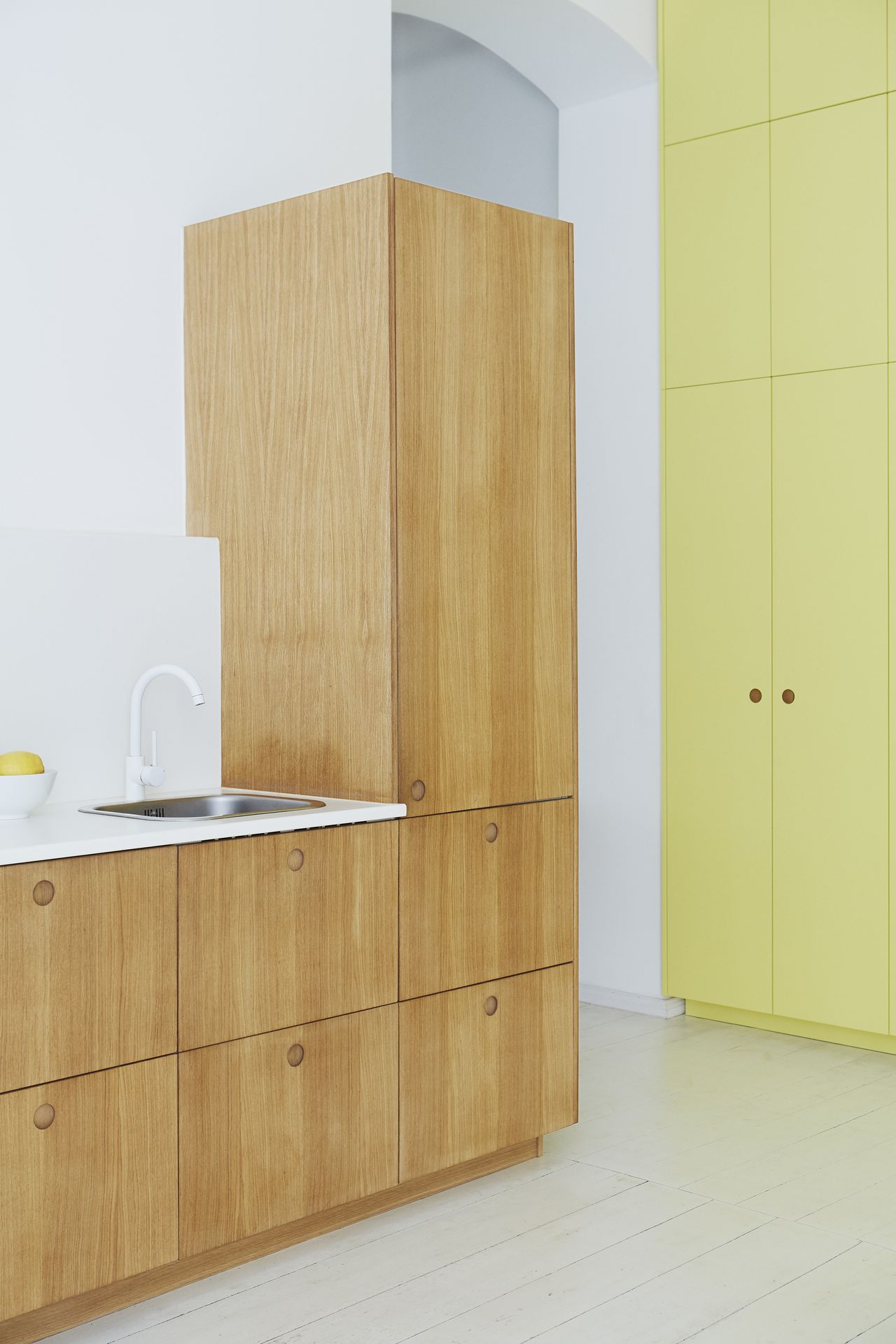 tangy yellow kitchen cabinets, timber galley kitchen with white countertops, white tap, white walls, and painted white floorboards