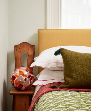 bedroom with yellow headboard, green patterned throw and globe light