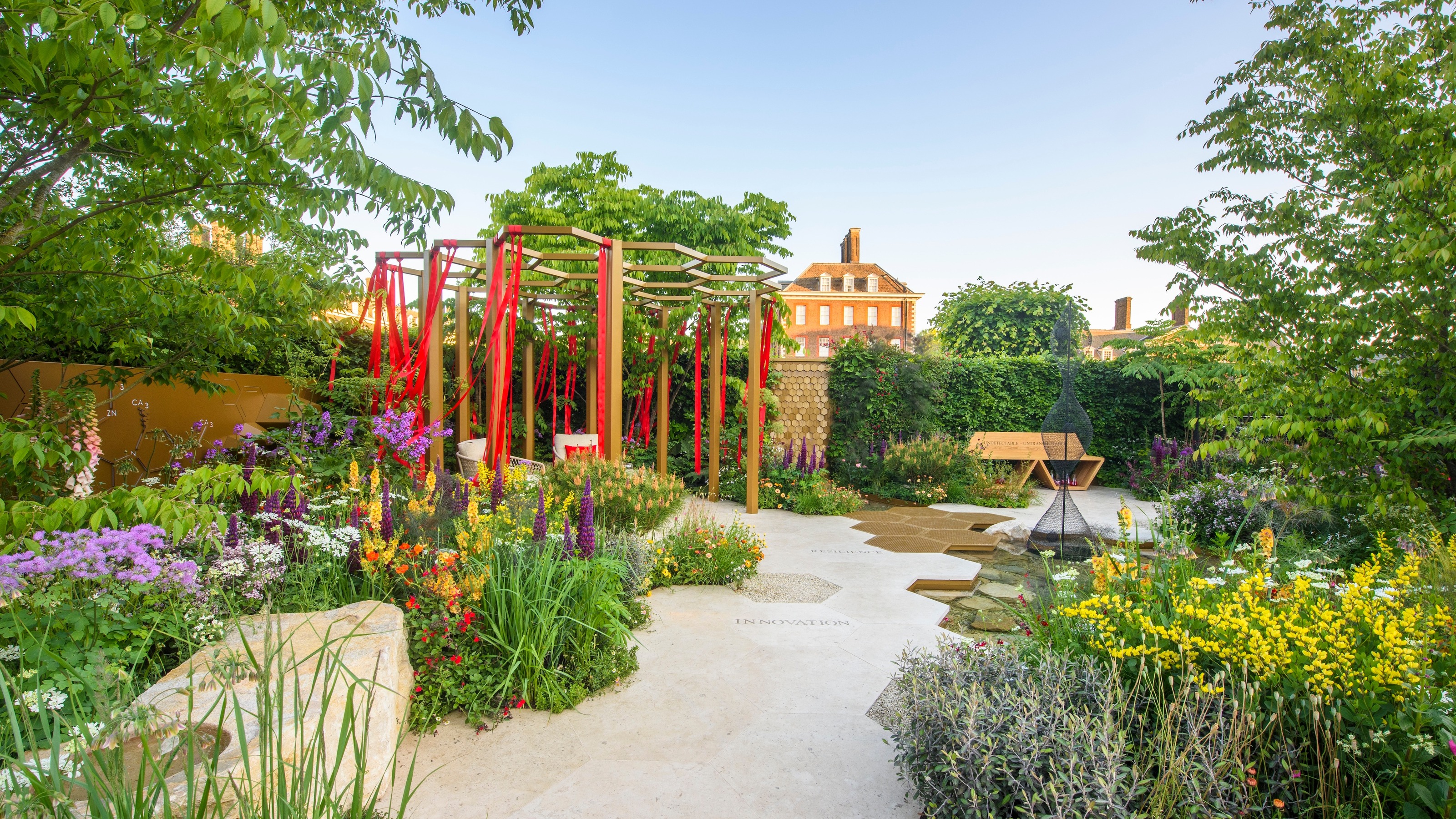 hexagonal pathway leading to pergola strewn with red ribbons at Chelsea Flower Show
