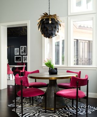 dining room with white walls, bright pink dining chairs and zebra-print rug