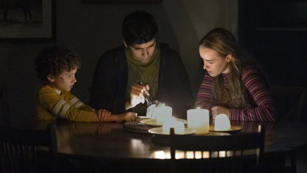 Three kids sit around a table with candles and torches 