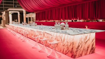 A room with pink curtain drapings and a 16-meter-long marble table with a row of transparent stools along the side