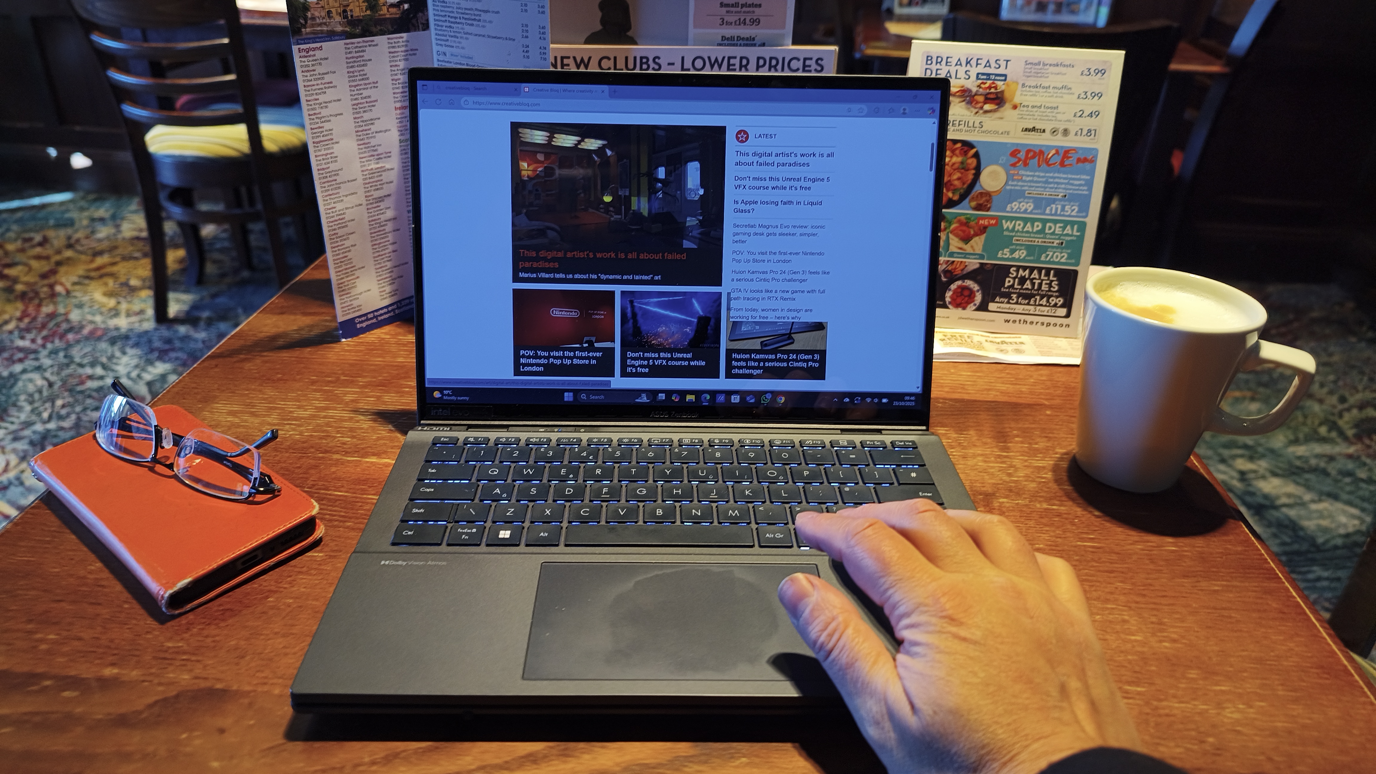A person's hand is resting near the trackpad of the laptop set up in a traditional mode, which is displaying a webpage on its single screen.