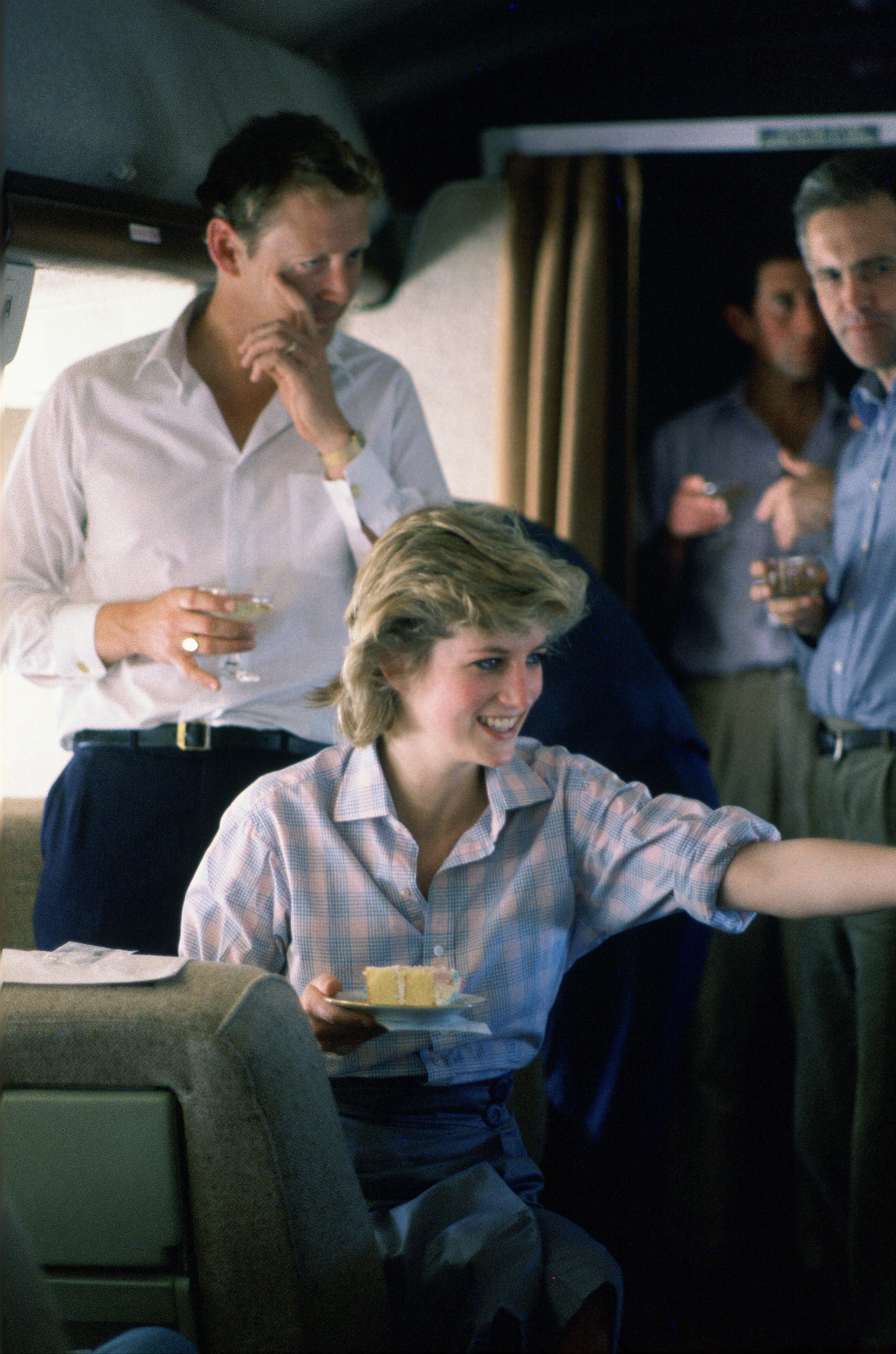 Princess Diana sitting on a plane eating a piece of cake