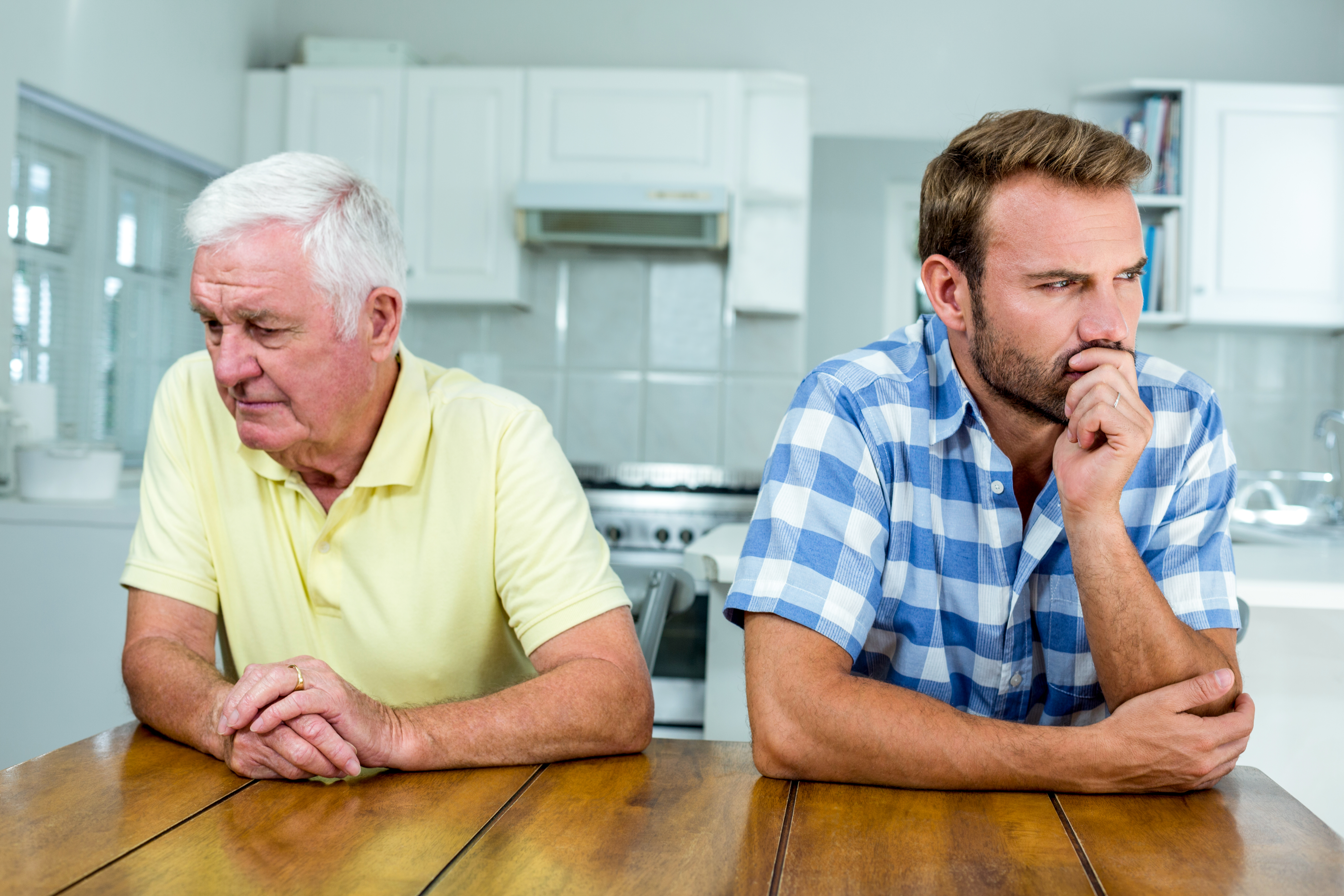 Close-up of tensed father and son sitting at table in kitchen