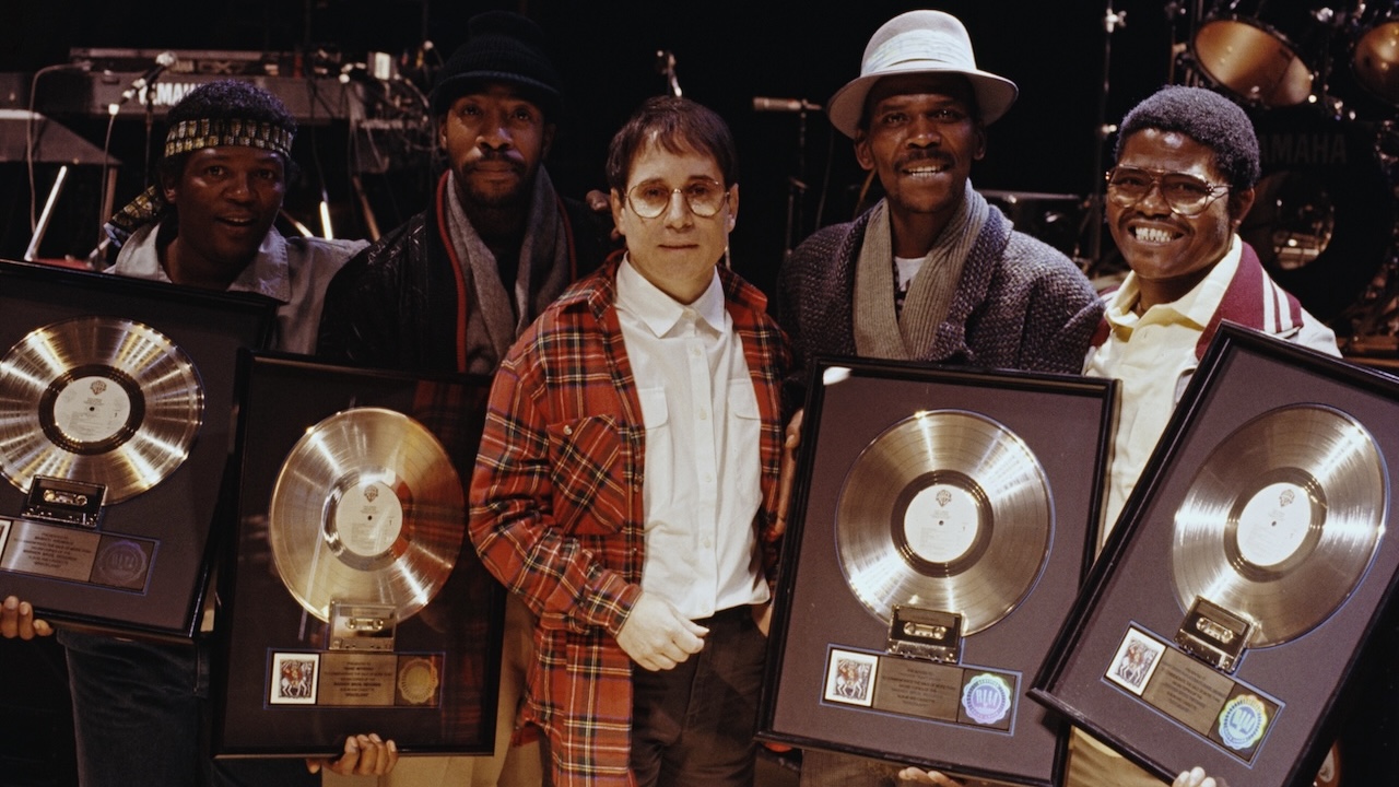 American singer-songwriter Paul Simon of folk rock duo Simon & Garfunkel posed with four musicians, all holding gold discs of Paul Simon's album Graceland, on which they contributed, London, 1987. 