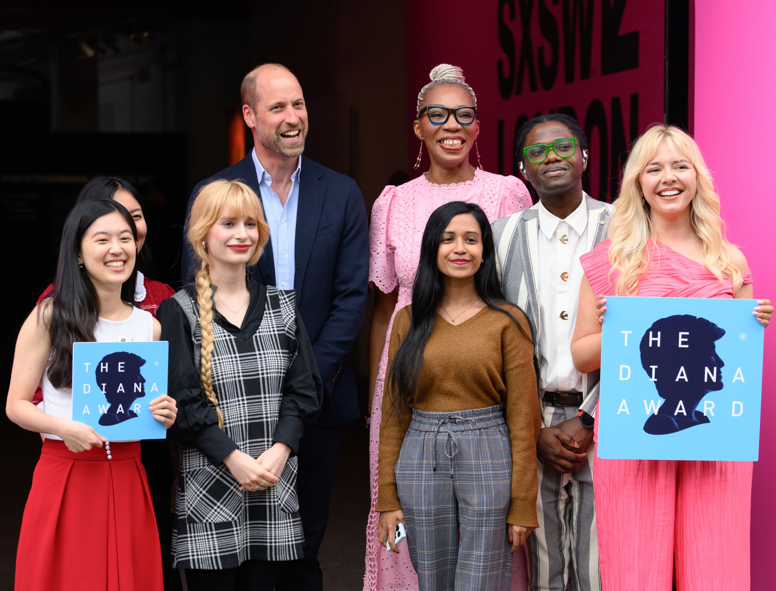 Prince William posing with Diana Award attendees holding up signs with the Diana Award logo