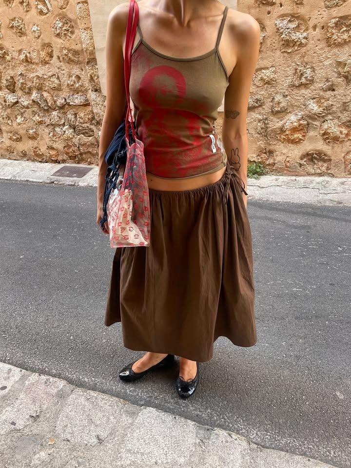 Influencer Susie Garvie wears a brown skirt and graphic tank with black flats.