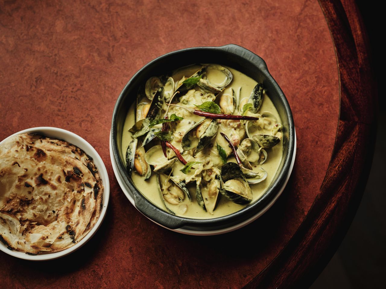 Aerial view of a curry dish and a pita, both served in round bowls.
