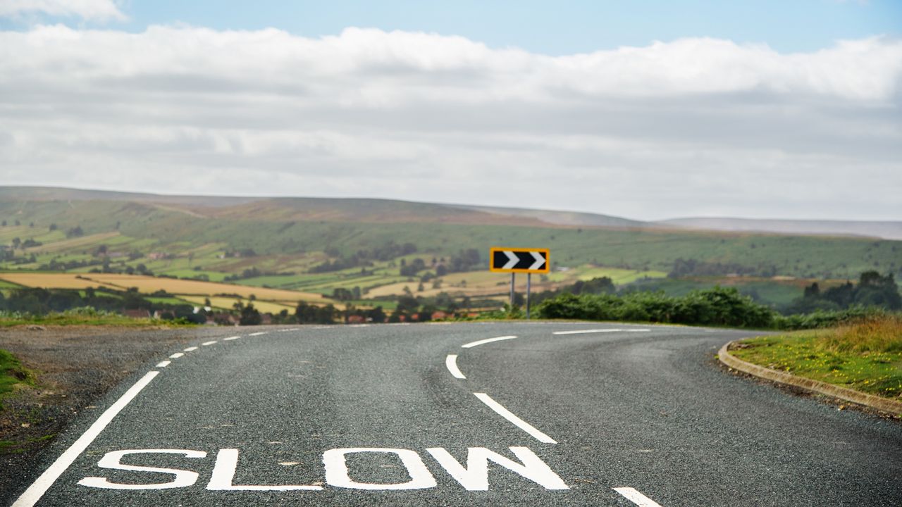 The word slow is painted on the pavement before a tight curve in the road.