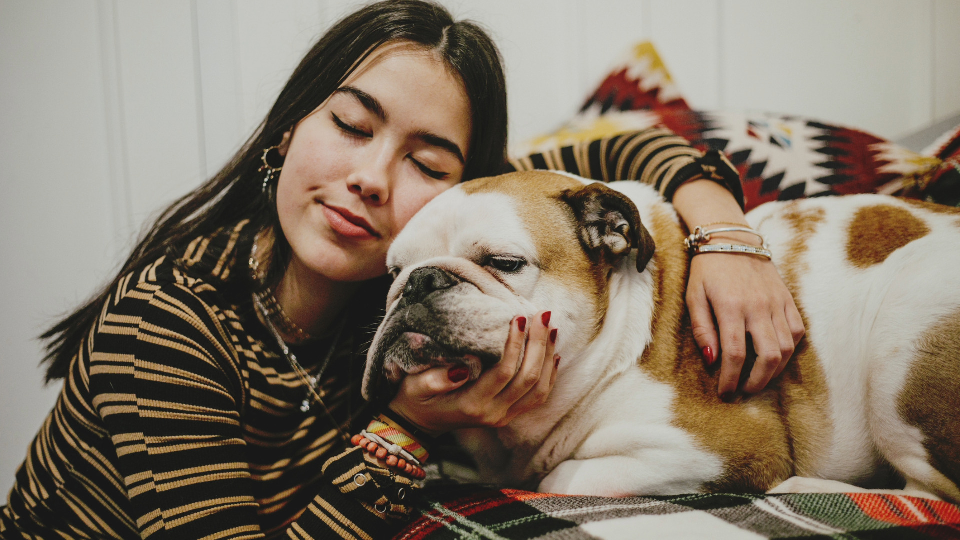 woman with closed eyes holds her face against a relaxed English bulldog