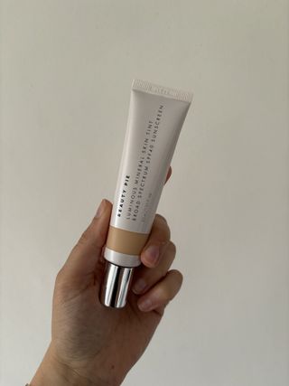 mica holding a tube of Beauty Pie Luminous Mineral Skin Tint Broad-Spectrum SPF 40 Sunscreen