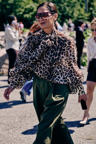 A woman crossing the street in a cheetah print top and green pants t new york fashion week