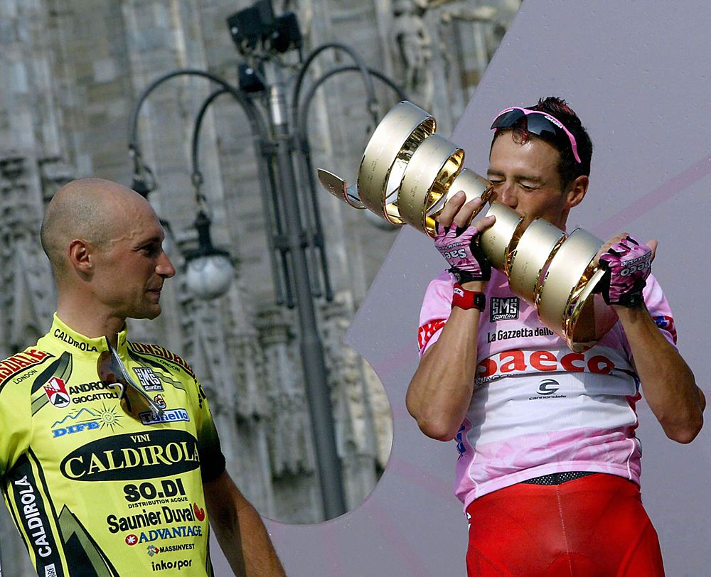 The 2003 Giro overall winner Italian Gilberto Simoni kisses the trophy as Stefano Garzelli looks on