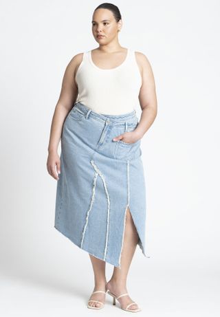 model wears white tank and asymmetrical denim skirt with white slide heels