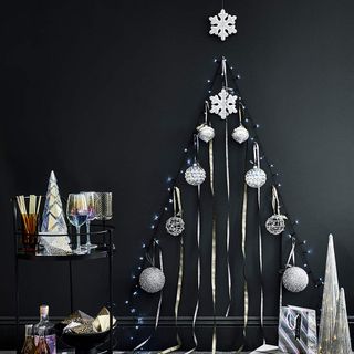 Fairy lights, ribbons and baubles in the shape of a Christmas tree on dark grey wall