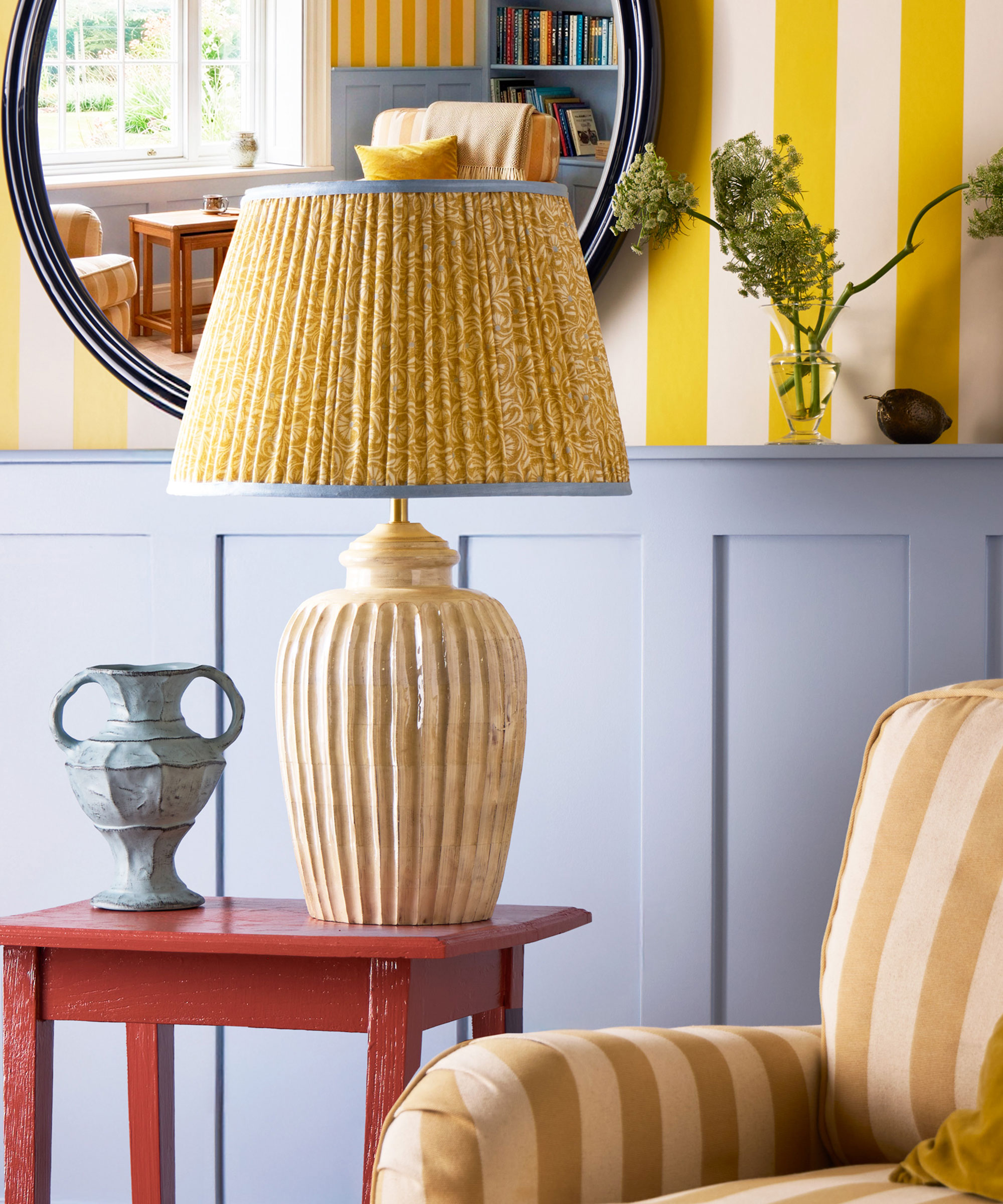 living room with blue half wall panelling and yellow and white striped wallpaper and oversized yellow table lamp