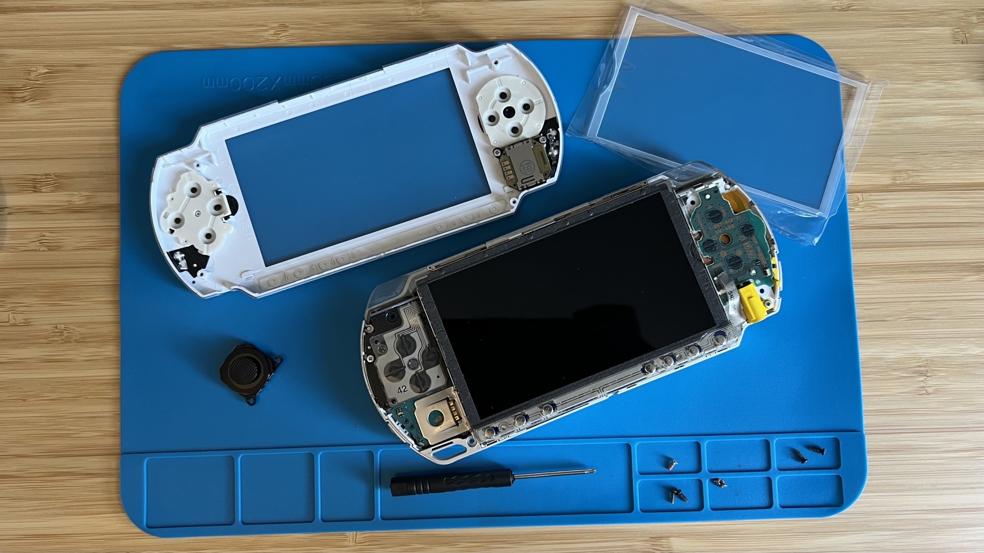 PSP with faceplate removed on a blue board with spare screen and thumbstick components
