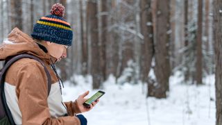 Man walking in snowy woods looking down at phone