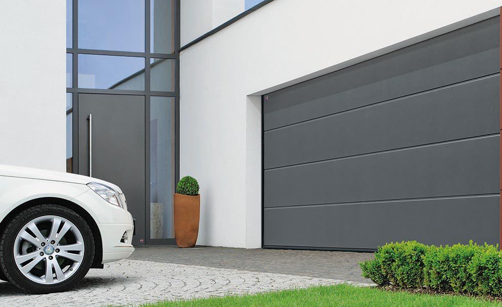 A grey garage door on a white garage